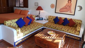 Une pièce comprenant un lit, deux canapés recouverts d’un tissu à motifs, une petite table avec un bol, une lampe et un tableau encadré accroché au mur.