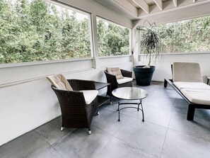 A covered patio with wicker furniture, a round table, and a potted plant.