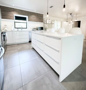 Une cuisine moderne avec des meubles blancs, un grand îlot central et un four encastré.