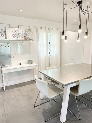 Une cuisine moderne avec un plan de travail blanc, un four encastré et un coin repas comprenant une grande table et des chaises blanches.