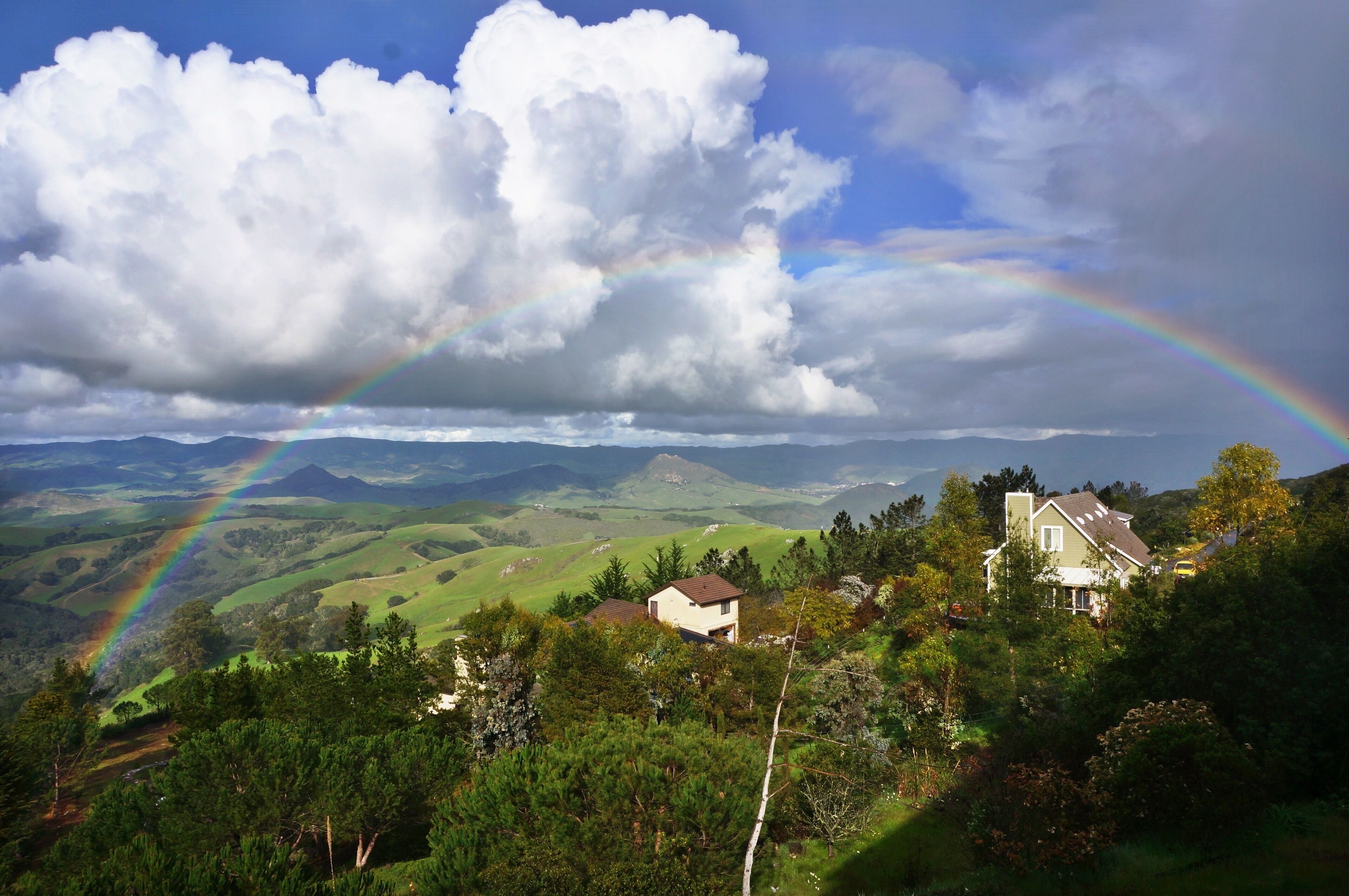 A house with a view of rolling hills and a rainbow.