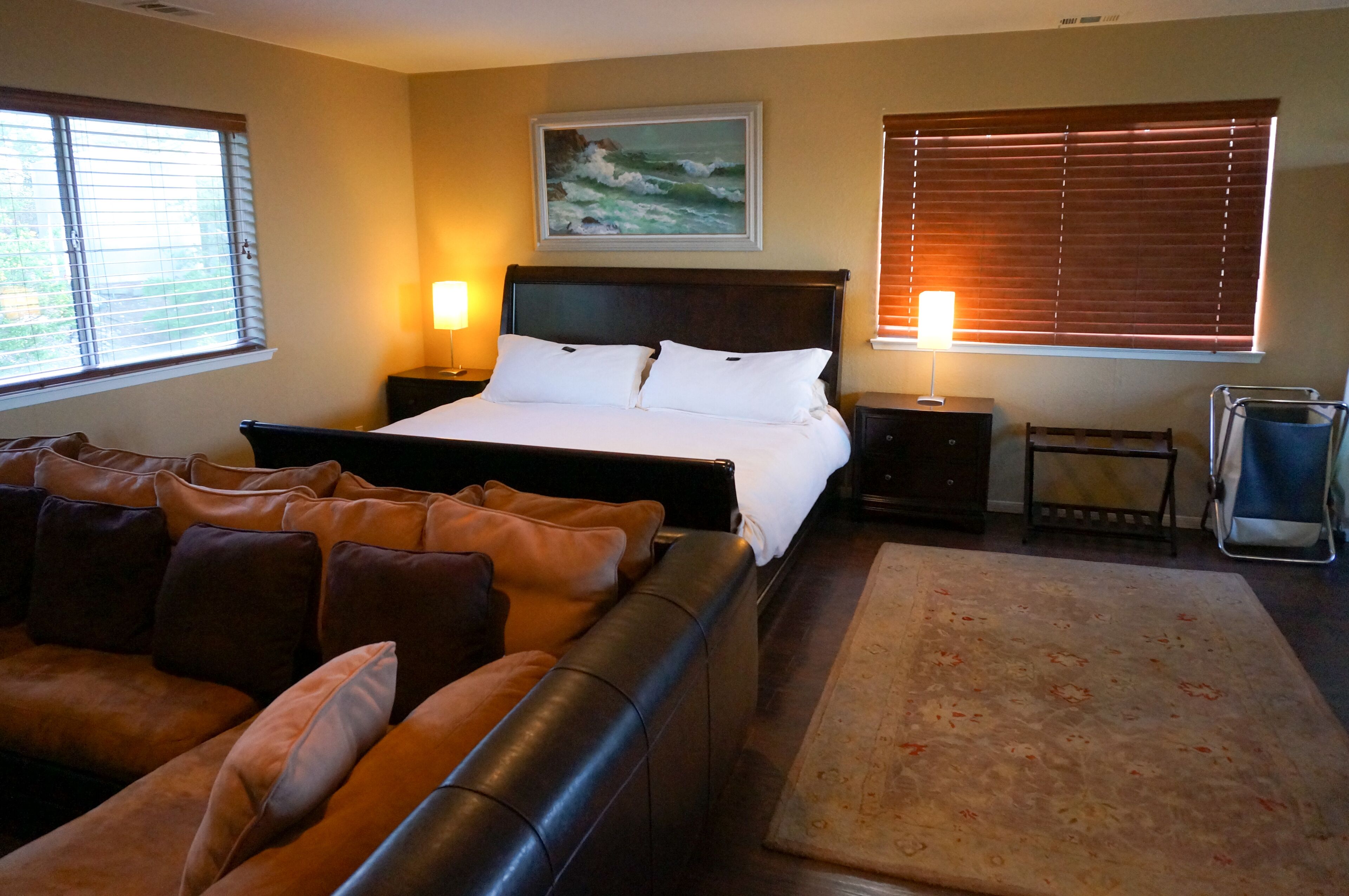 A hotel room with a bed, a sofa, a painting, and two lamps.