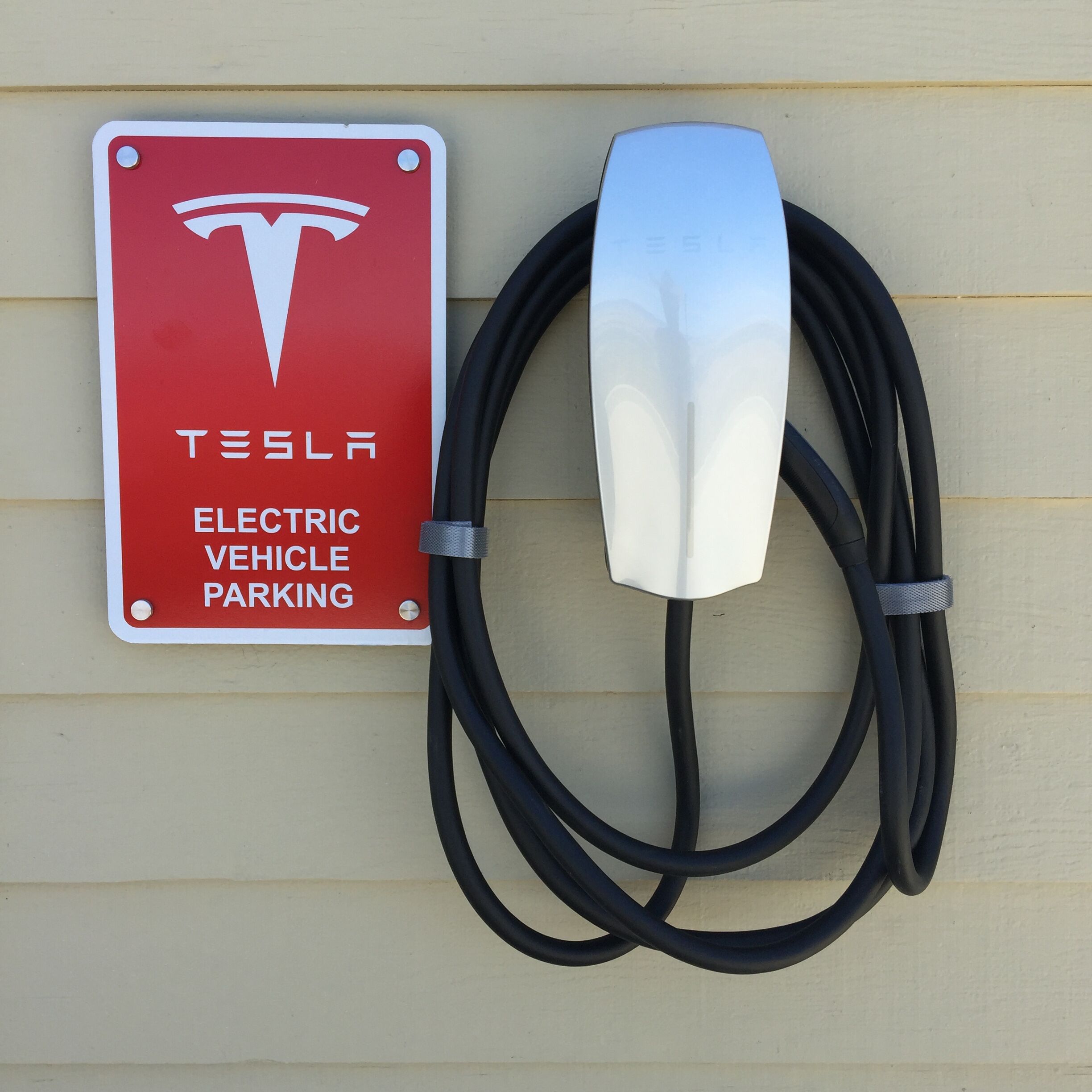 Een Tesla elektrische auto laadstation met een rood bord en een witte laadpaal.