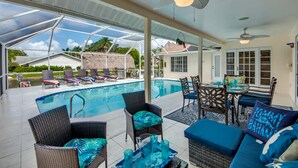 Zona de piscina exterior con sillones de descanso, una mesa de comedor y ventiladores de techo.