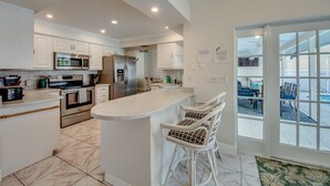 Una cocina moderna con armarios blancos, electrodomésticos de acero inoxidable y una zona de bar con sillas de mimbre blanco.
