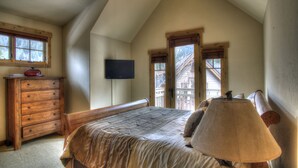 Una camera da letto con soffitto spiovente, comò in legno, letto con cuscini e una lampada.