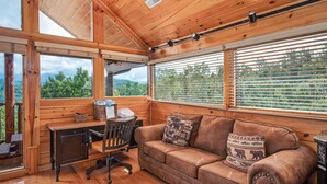 Ein Holzhütten-Interieur mit einem Holztisch, einer Ledercouch und großen Fenstern mit Blick auf Grünflächen.