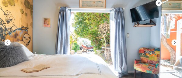 A bedroom with a bed, a TV, a chair, and a view of the outdoors.