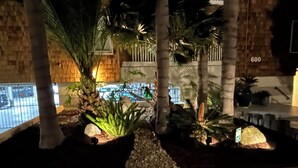 Une vue nocturne d’un bâtiment avec une piscine, des palmiers et un mur en pierre.