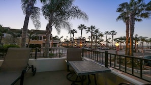 A balcony with chairs and a table, overlooking a street lined with palm trees and buildings.