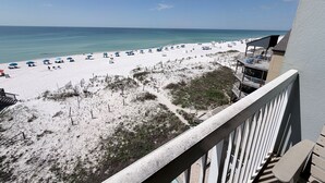 A beach view from a balcony with a railing, a sandy beach, and a clear blue sky.