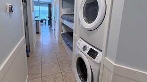 A laundry room with stacked washers and dryers, a tiled floor, and a view to a balcony.