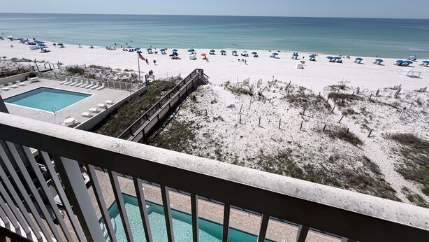 A beach view with a pool, beach chairs, and umbrellas.