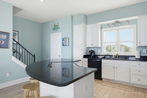 A kitchen with a black countertop, white cabinets, a coffee maker, and a window with blinds. - 🌞Oceanfront 🏖️Steps to sand 🐶Dog Friendly⚡️EV charger (North Topsail Beach)