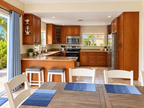 A modern kitchen with wooden cabinets, a central island, and a dining area with chairs and a table.