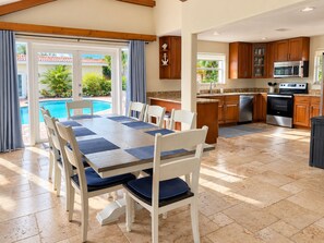 A dining area with a pool view, a kitchen with modern appliances, and wooden cabinets.