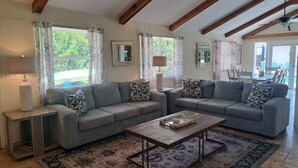 A living room with a grey sofa, a wooden coffee table, patterned rugs, and a ceiling fan. -  Closest To Beach Main House & Separate Villa 4 Bdrm , Huge Pool. Walk To Beach (Naples)