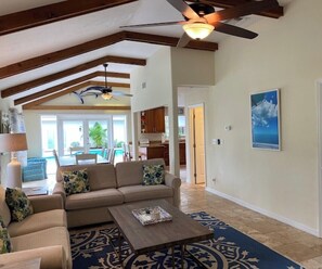 Cozy living area with a high ceiling, sofa, armchair, and coffee table, opening to a kitchen and dining space.