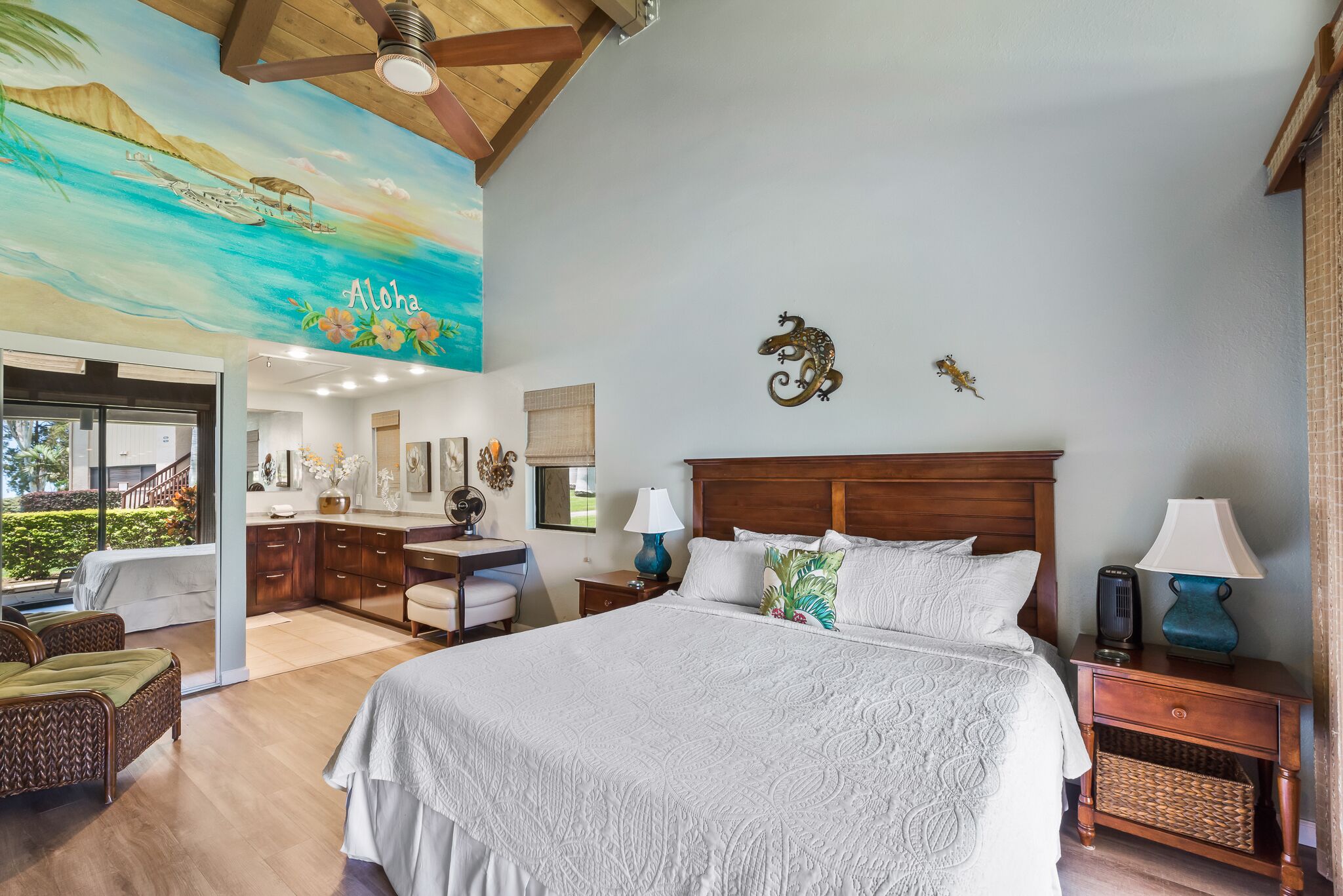 A spacious bedroom with a large bed, wooden headboard, and a ceiling mural depicting a tropical scene.