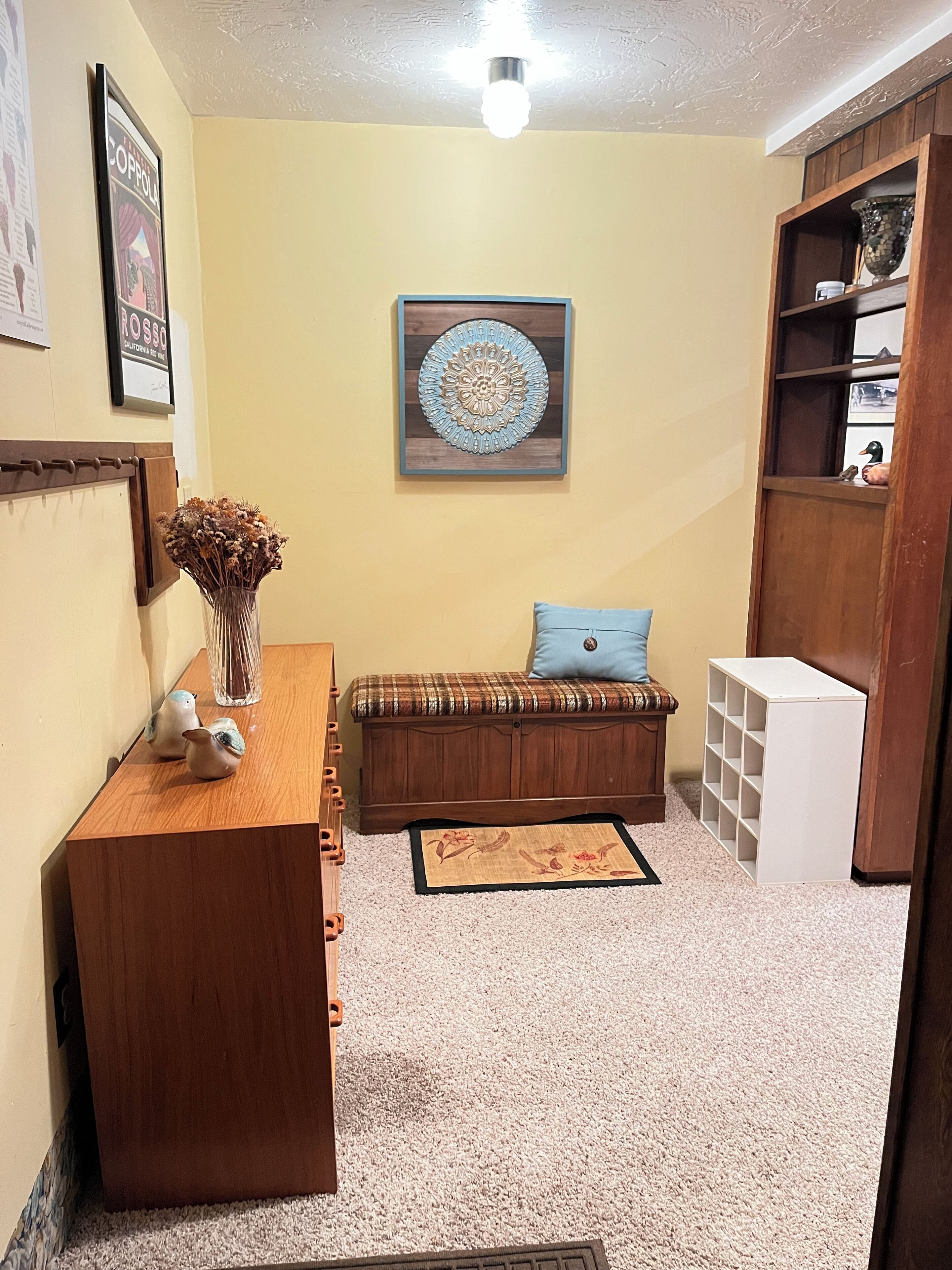 Una stanza accogliente con una scrivania in legno, una panca con cuscino a quadri, un elemento decorativo a parete e una libreria.