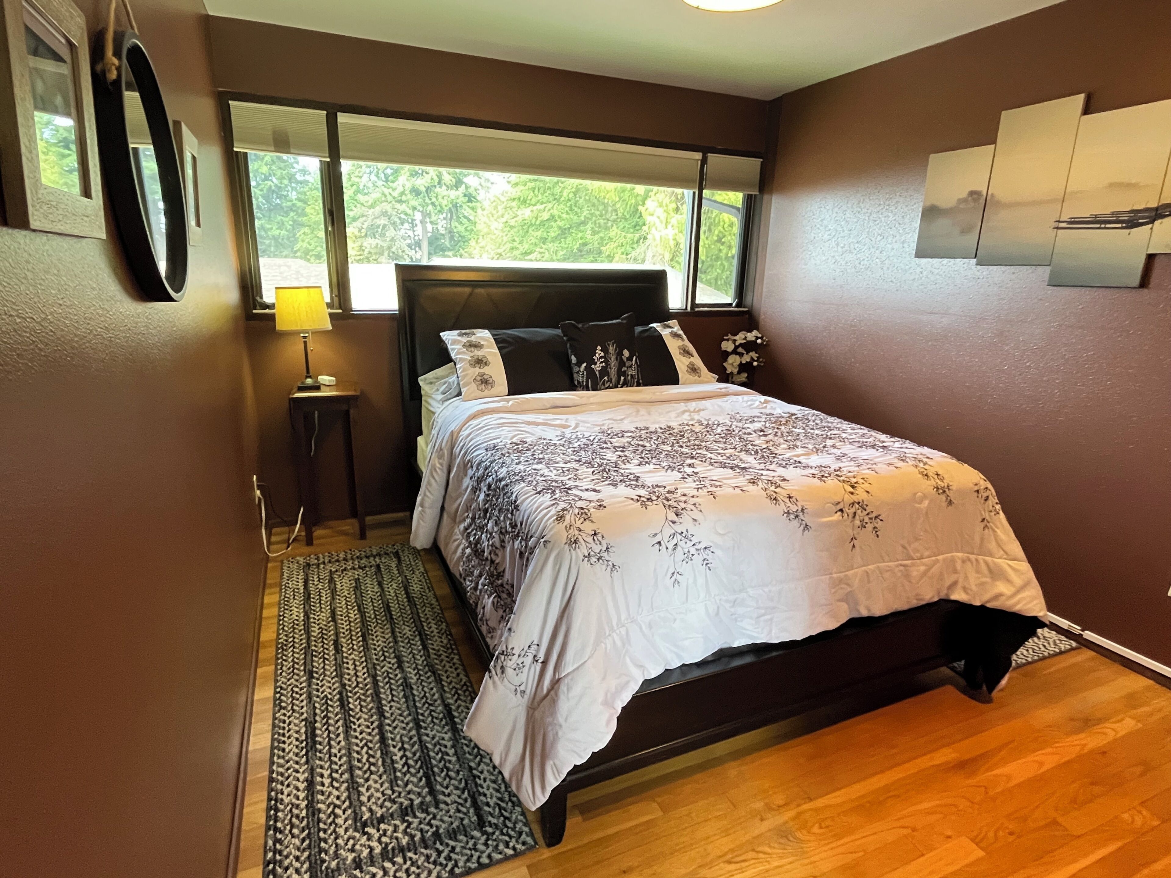 A bedroom with a bed, a bedside table, a lamp, a window, and a rug.