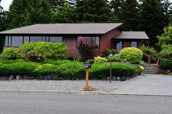 A two-story house with a dark roof and large windows, surrounded by well-maintained greenery and a mailbox. - Immaculate, warm, inviting with WOW water views! You'll wish you lived here! (Port Angeles)