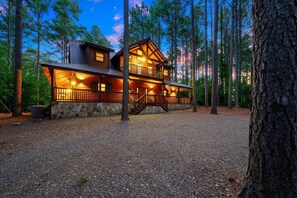 Escape to a serene forest retreat with a covered porch and staircase leading to a cozy upstairs area.