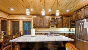 Una cucina con mobili in legno, un piano di lavoro in granito, un frigorifero in acciaio inossidabile e un angolo bar con sgabelli.