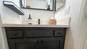 A bathroom with a white countertop, black cabinets, a mirror, and a bottle of hand sanitizer.