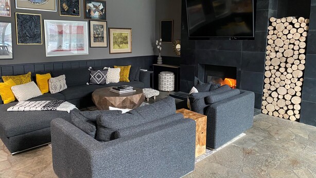 A modern living room with a grey sectional sofa, a round coffee table, and a fireplace with stacked logs.