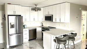 A modern kitchen with white cabinets, stainless steel appliances, a marble countertop, and a bar area with stools.