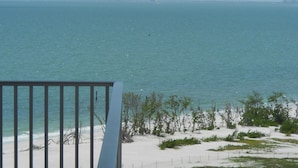 A view of a beach with a railing in the foreground, sandy shore, and the ocean.