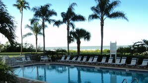 A pool area with lounge chairs and palm trees, a sign, and a view of the ocean.