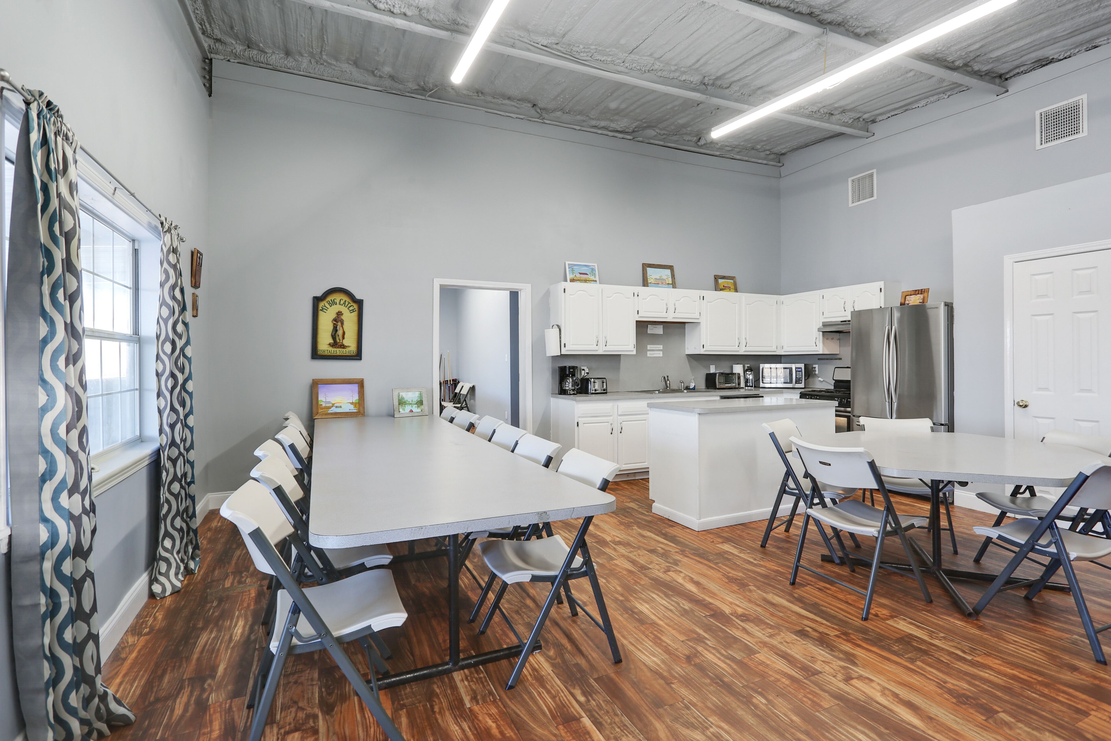 A modern kitchen with white cabinets, a stainless steel refrigerator, and a dining area with a large table and chairs.