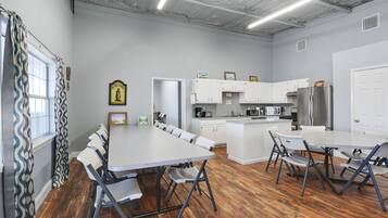 A modern kitchen with white cabinets, a stainless steel refrigerator, and a dining area with a large table and chairs.