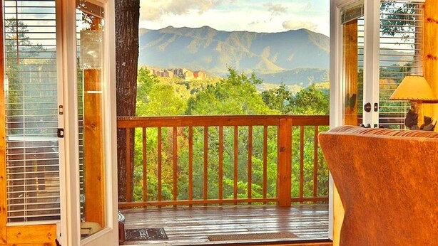 Eine Holzterrasse mit Blick auf Berge, ein Holzstuhl und eine Tür mit Glasfenstern.