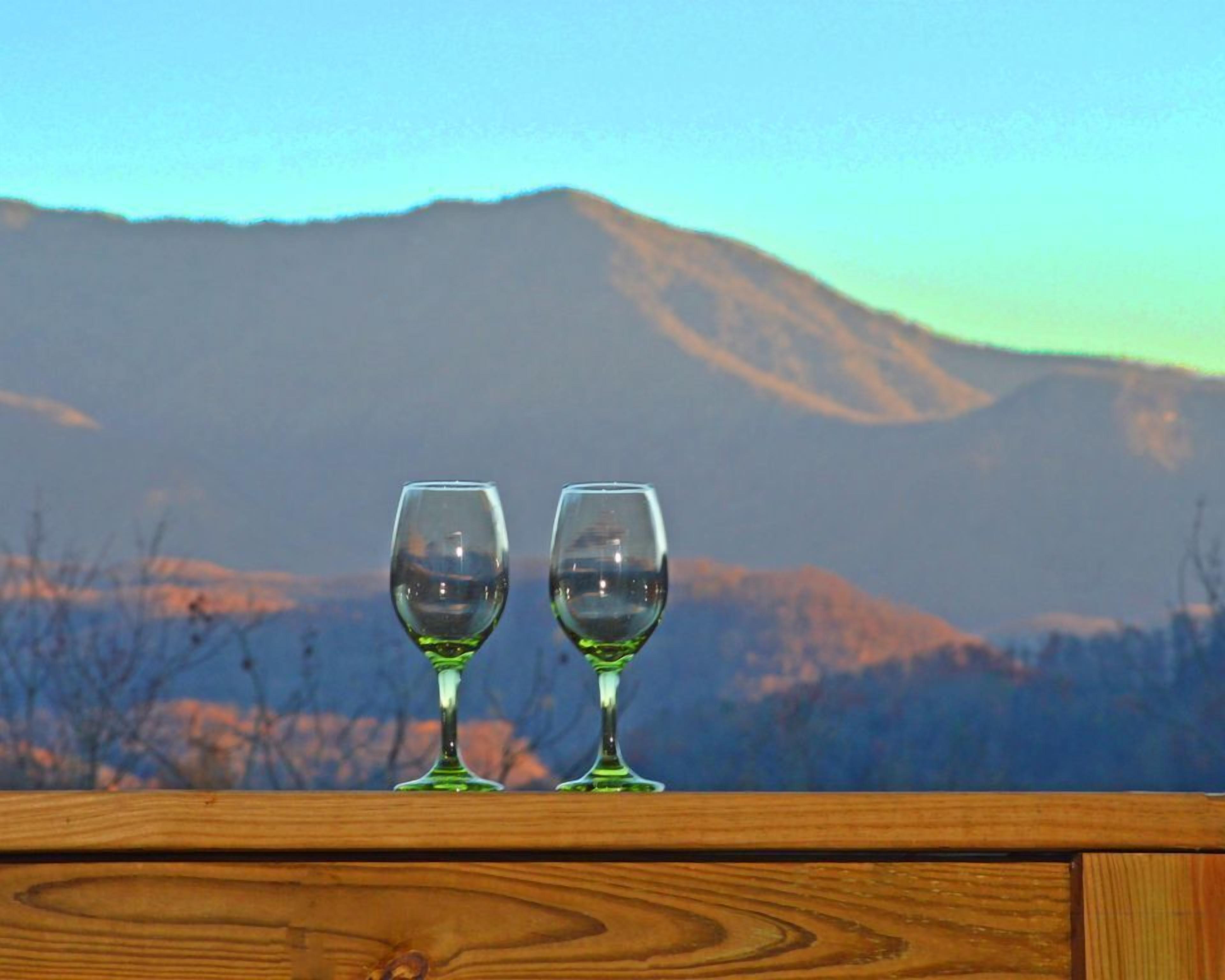 Two empty wine glasses on a wooden surface with a mountainous landscape in the background.