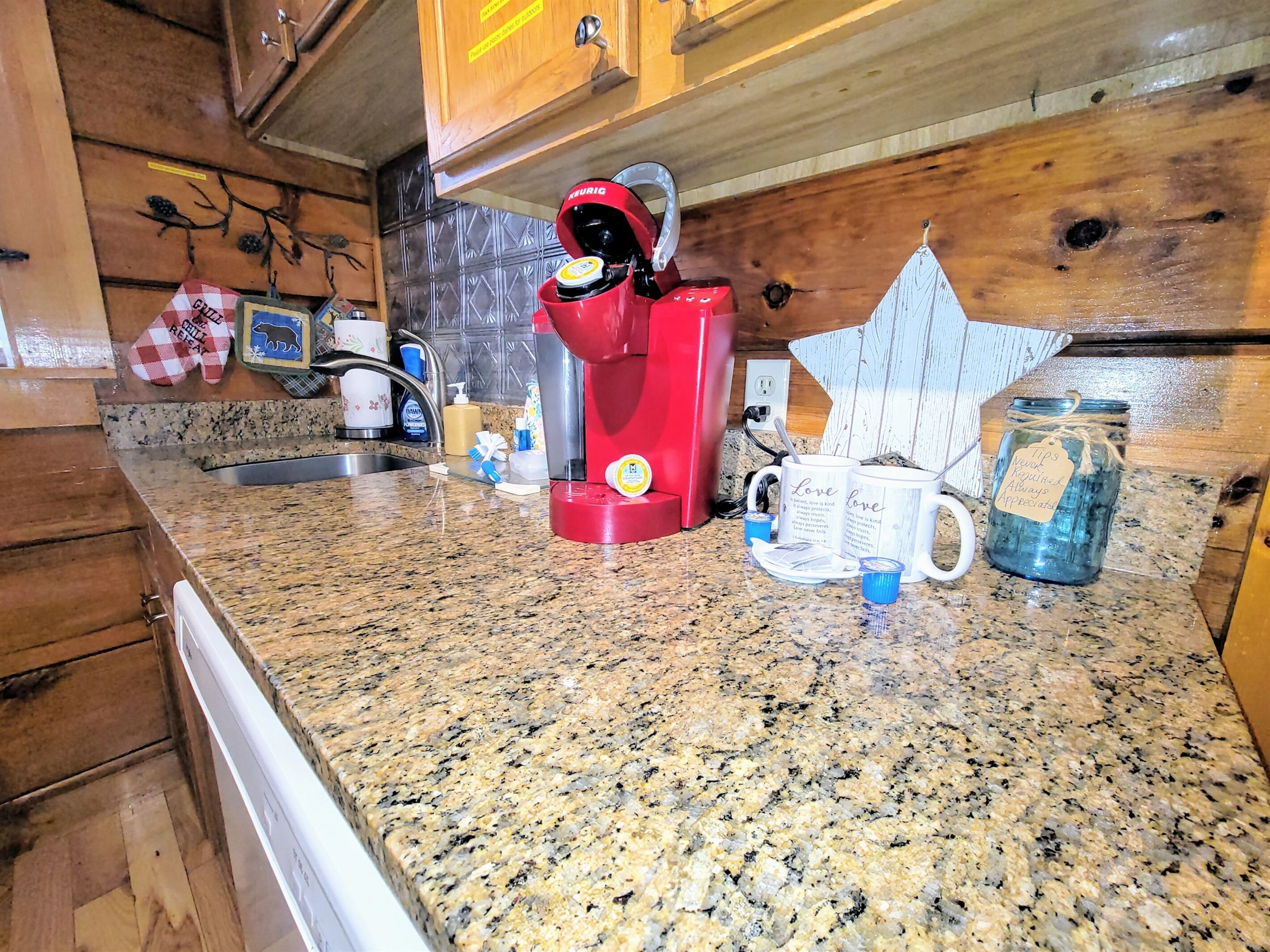 Una cocina con encimera de granito, una cafetera roja, un tarro con etiqueta y una taza con diseño de corazón.