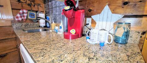Una cocina con encimera de granito, una cafetera roja, un tarro con etiqueta y una taza con diseño de corazón.
