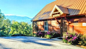 Eine Holzhütte mit einem 'WELCOME'-Schild, einer Veranda und Blick auf Berge.