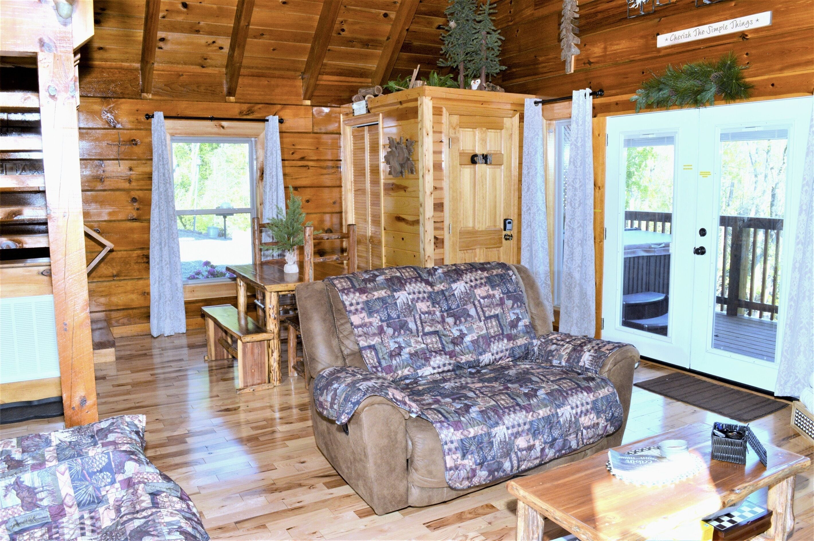 Ein gemütliches Blockhaus-Interieur mit Holzboden, einer Couch, einem Tisch und einer Tür, die nach draußen führt.