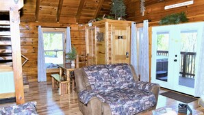 Ein gemütliches Blockhaus-Interieur mit Holzboden, einer Couch, einem Tisch und einer Tür, die nach draußen führt.