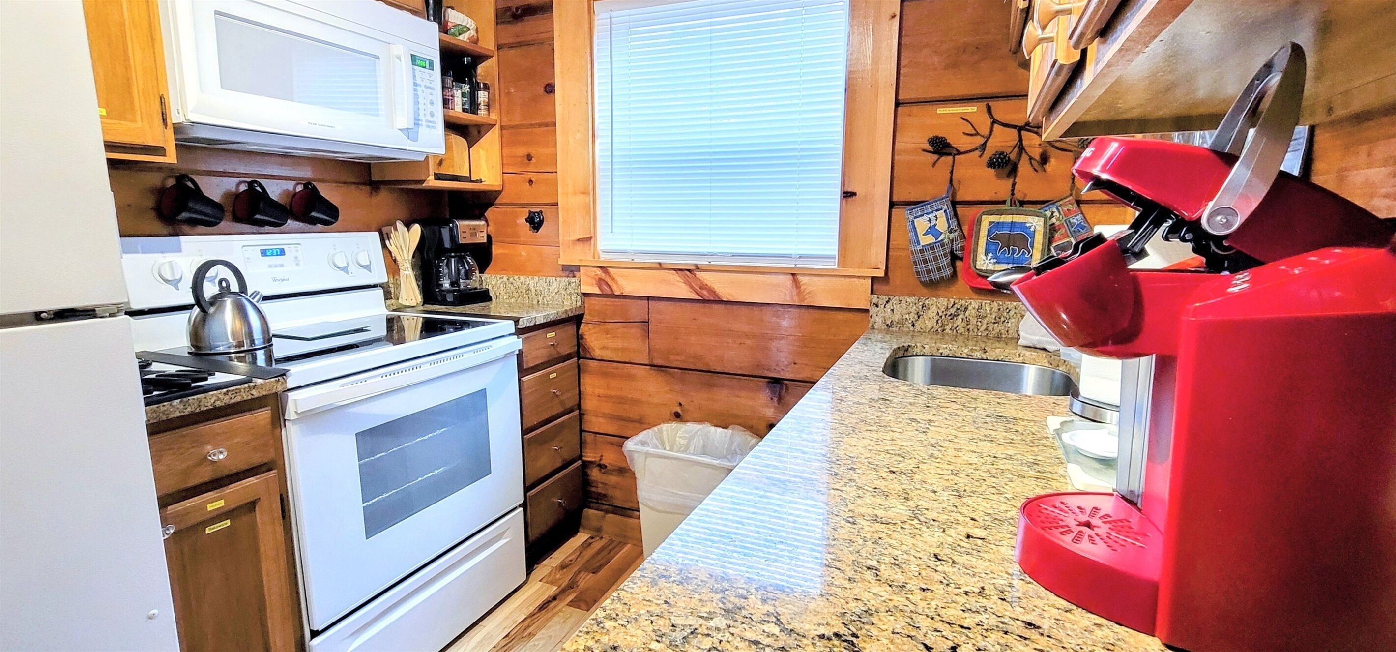 Une cuisine avec des meubles de rangement en bois, un four à micro-ondes, une cuisinière et une machine à café rouge.