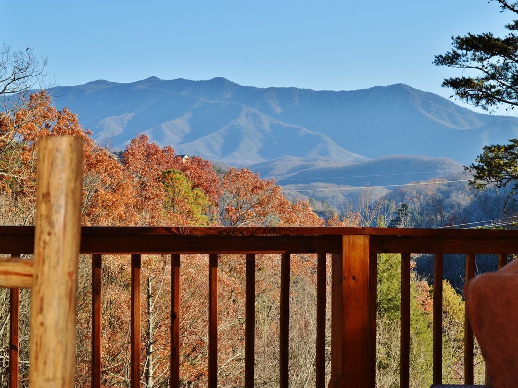 Terraza de madera con vistas al follaje otoñal y montañas a lo lejos.