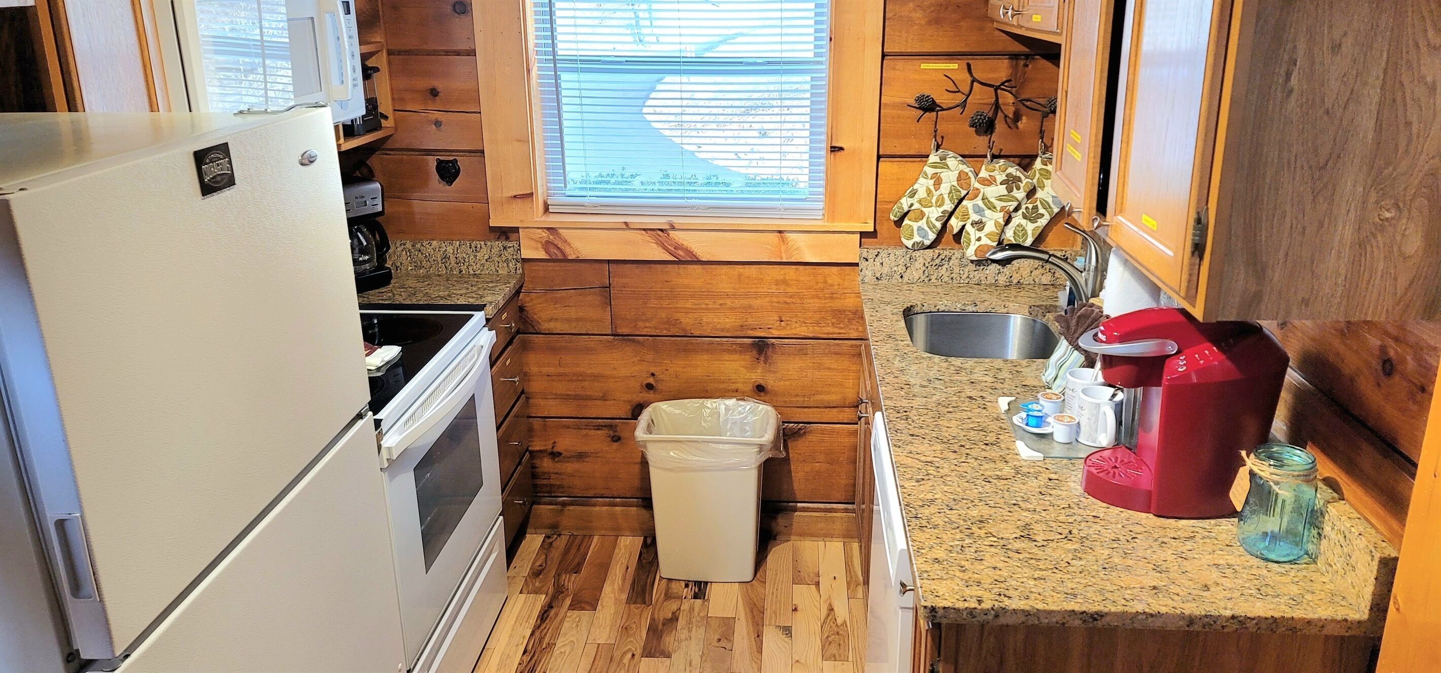 A compact kitchen with wooden walls, a white refrigerator, a stove, a sink, and a coffee maker.