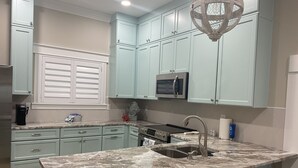 Una cocina con armarios azul claro, encimera de granito, pileta de acero inoxidable y microondas moderno.