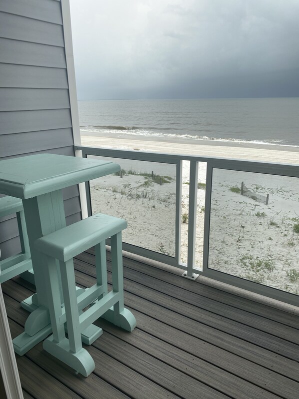Eine Holzterrasse mit Tisch und Bank mit Blick auf einen Strand.