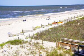Ein Strand mit einer Holzbrücke, einem Holzzaun und Liegestühlen.