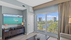 A modern living room with a large TV, a wooden coffee table, and a balcony with a view of the city and water.