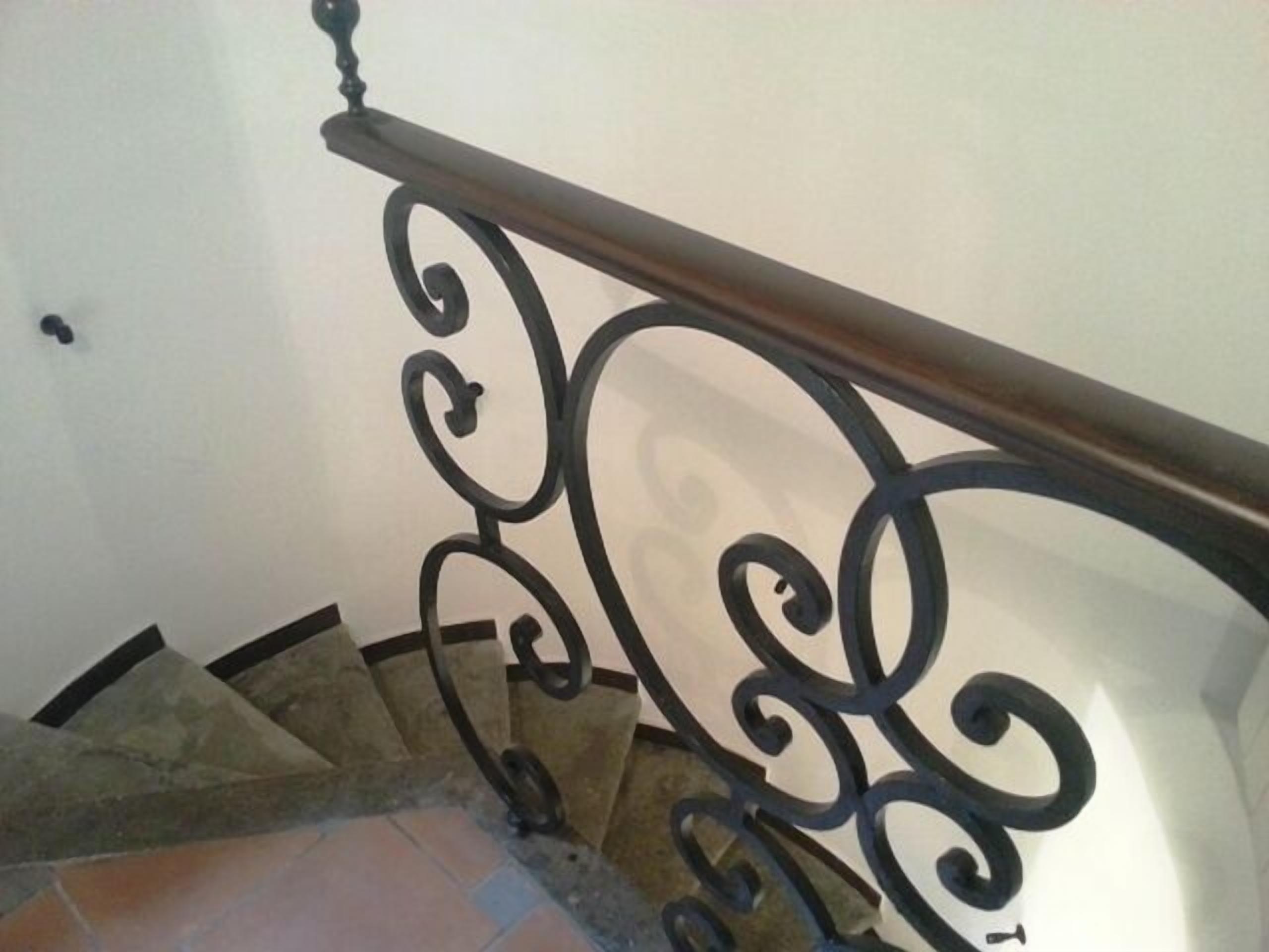 Eine Treppe mit aufwendiger schwarzer Metallreling und einem hölzernen Geländer.